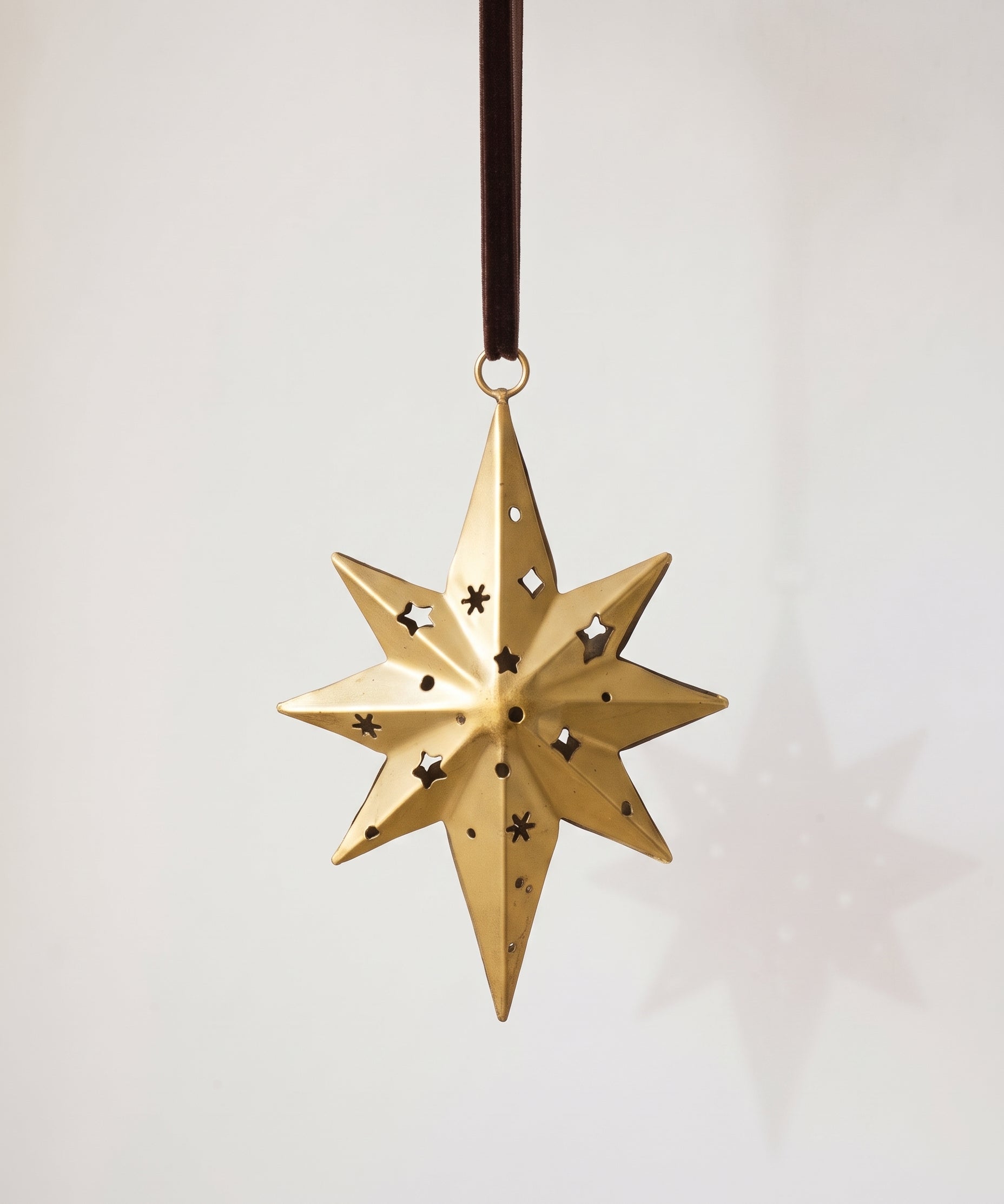 Gold hand-cut iron north star Christmas ornament with a long leading point, hung from a black velvet ribbon