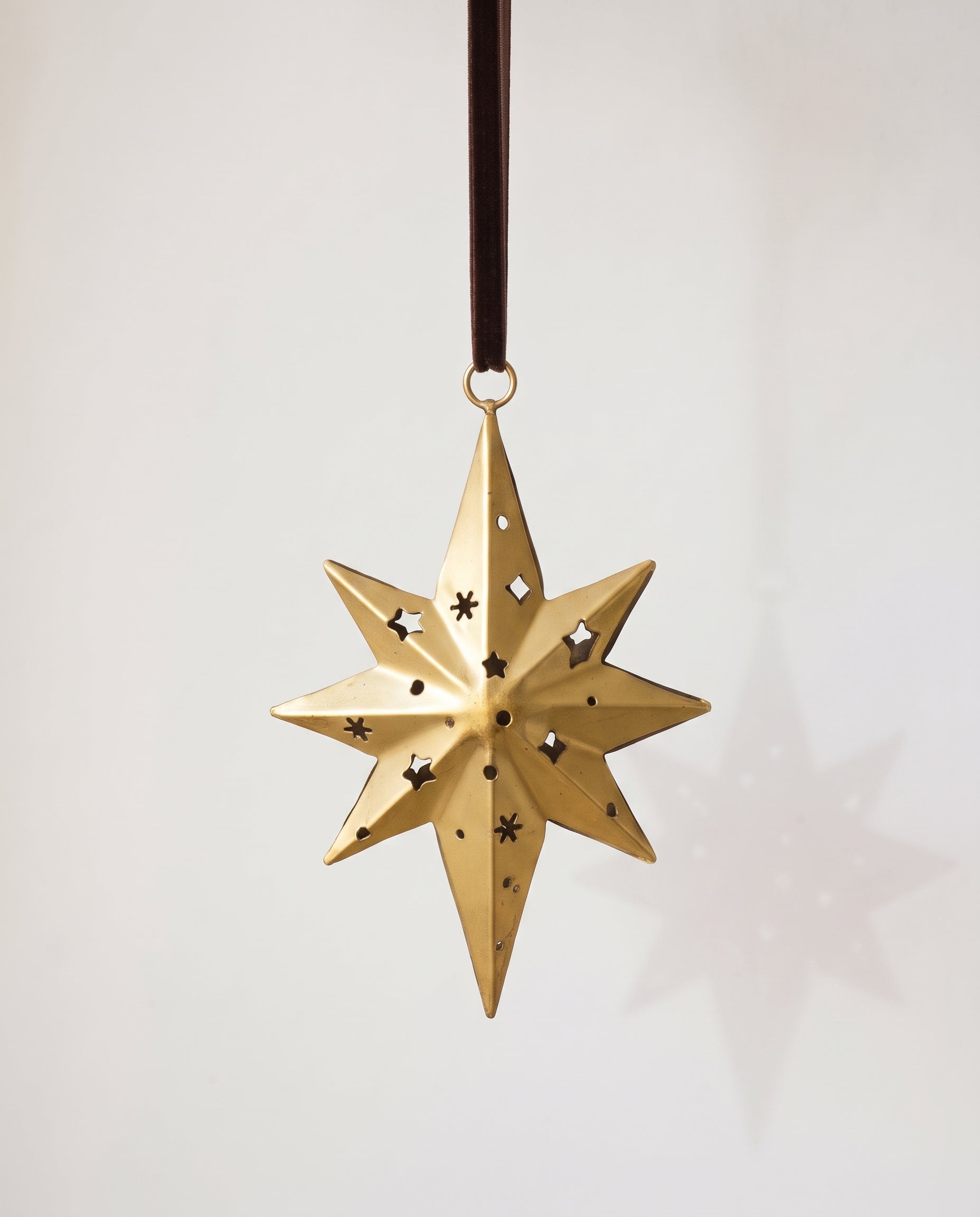 Gold hand-cut iron north star Christmas ornament with a long leading point, hung from a black velvet ribbon