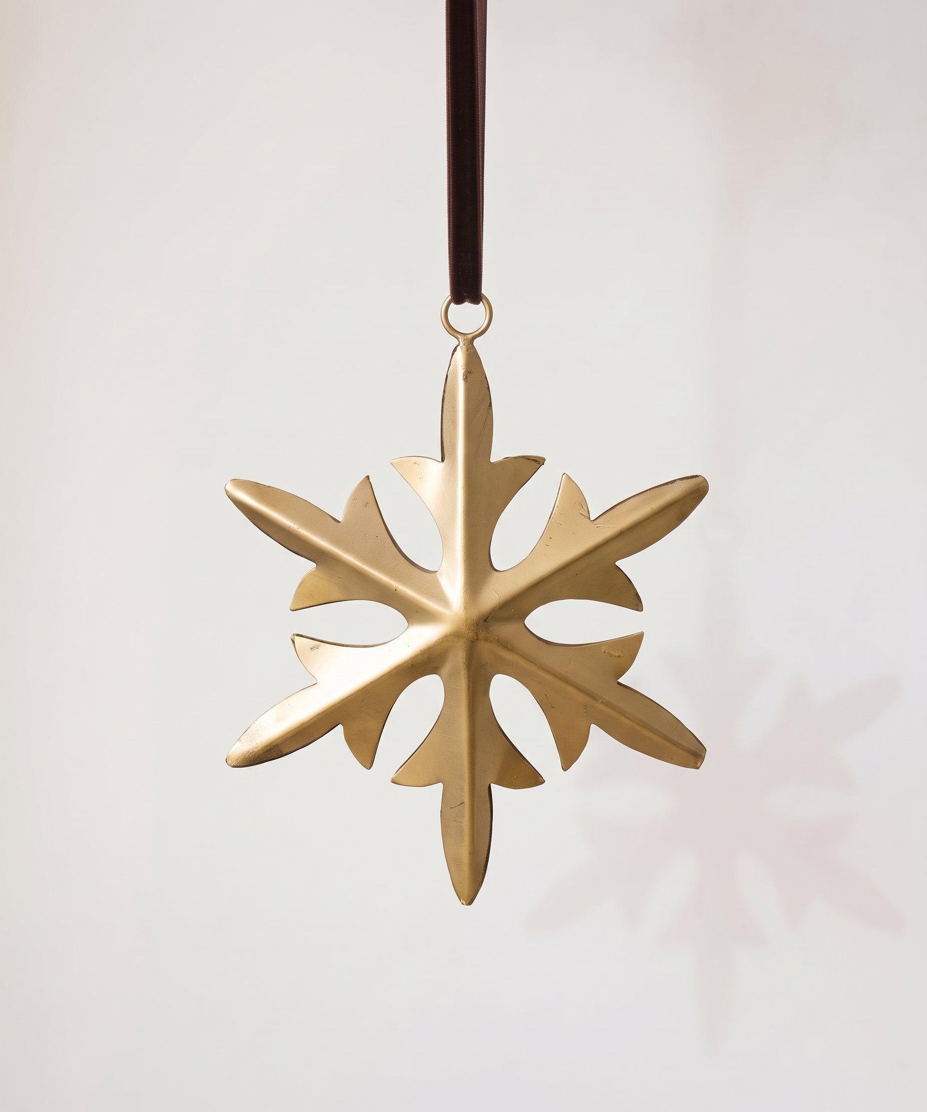 Gold hand-cut iron snowflake Christmas ornament with fine cut detail, hung from a black velvet ribbon