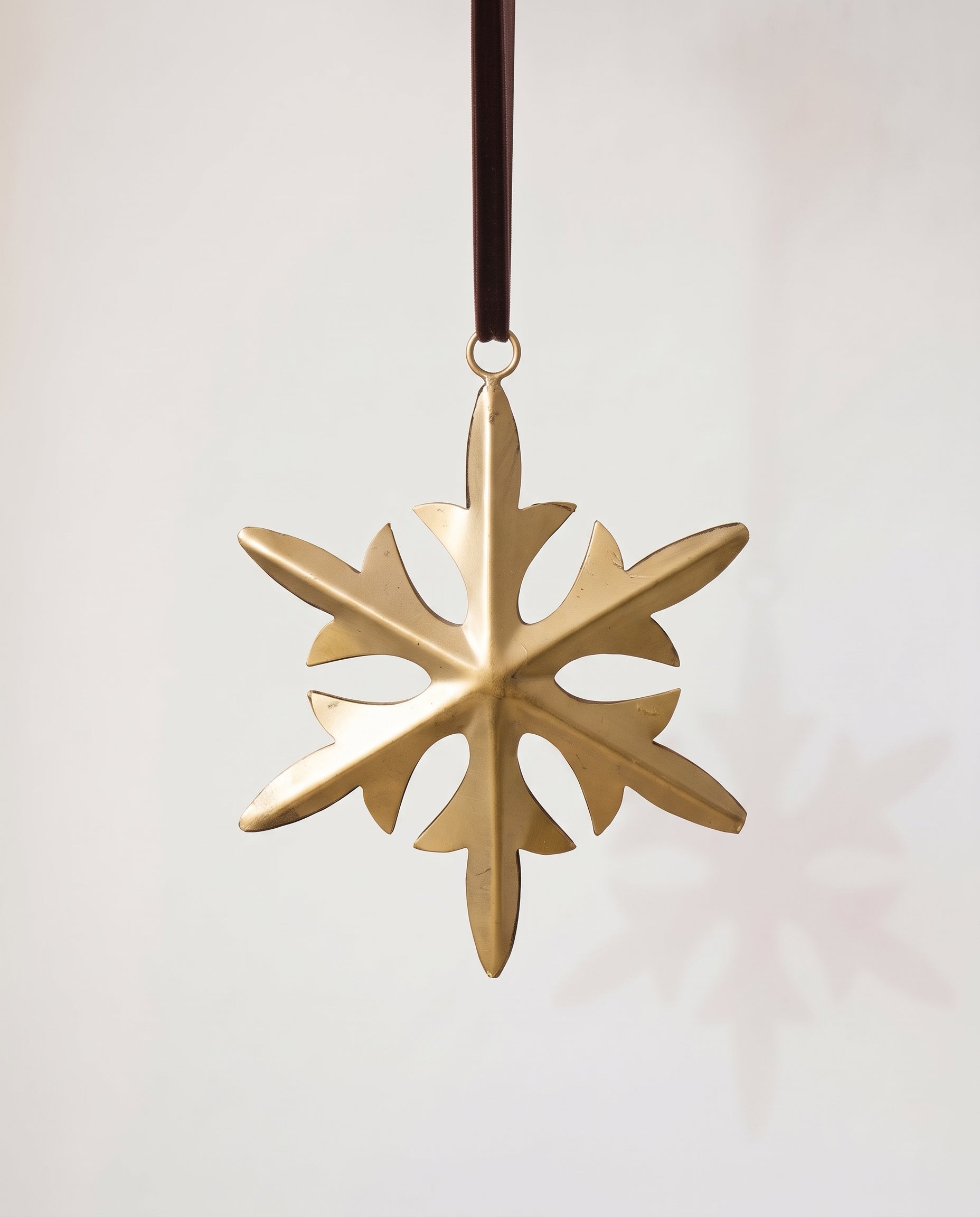Gold hand-cut iron snowflake Christmas ornament with fine cut detail, hung from a black velvet ribbon
