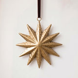 Gold hand-cut iron sunburst Christmas ornament with radiating rays, hung from a black velvet ribbon