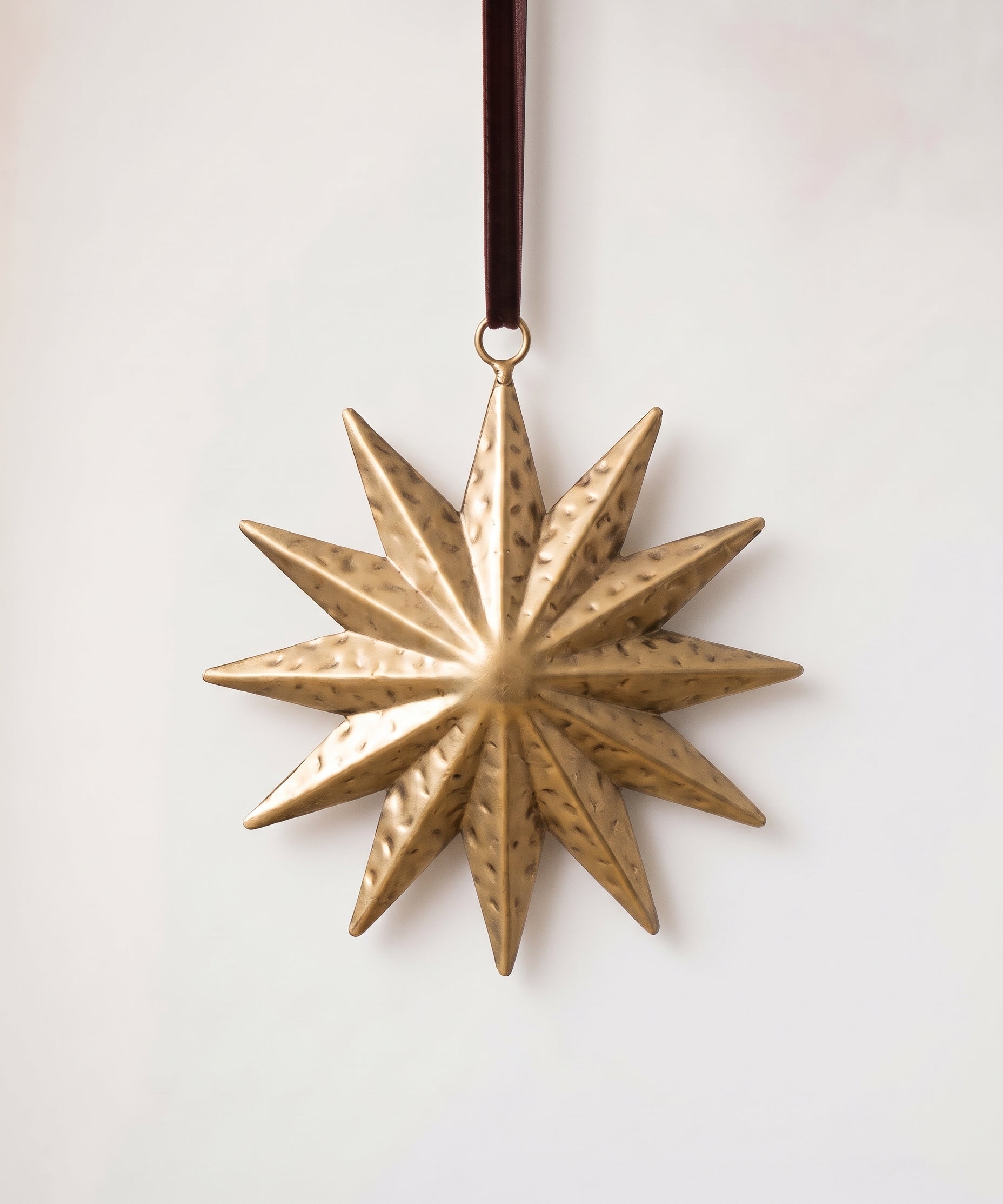 Gold hand-cut iron sunburst Christmas ornament with radiating rays, hung from a black velvet ribbon
