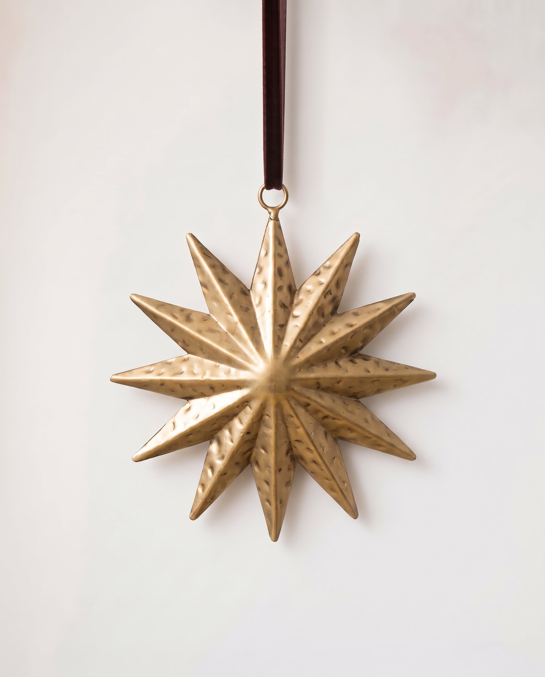 Gold hand-cut iron sunburst Christmas ornament with radiating rays, hung from a black velvet ribbon