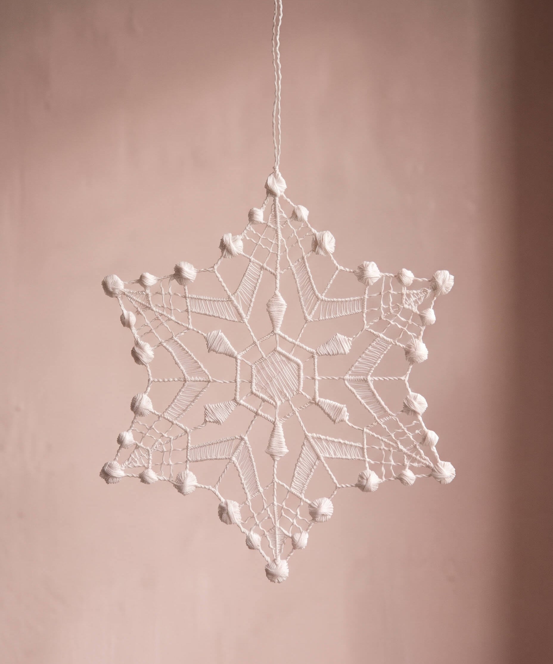 Six-point white Plauen lace snowflake ornament with dotted strands, made in Plauen, Germany