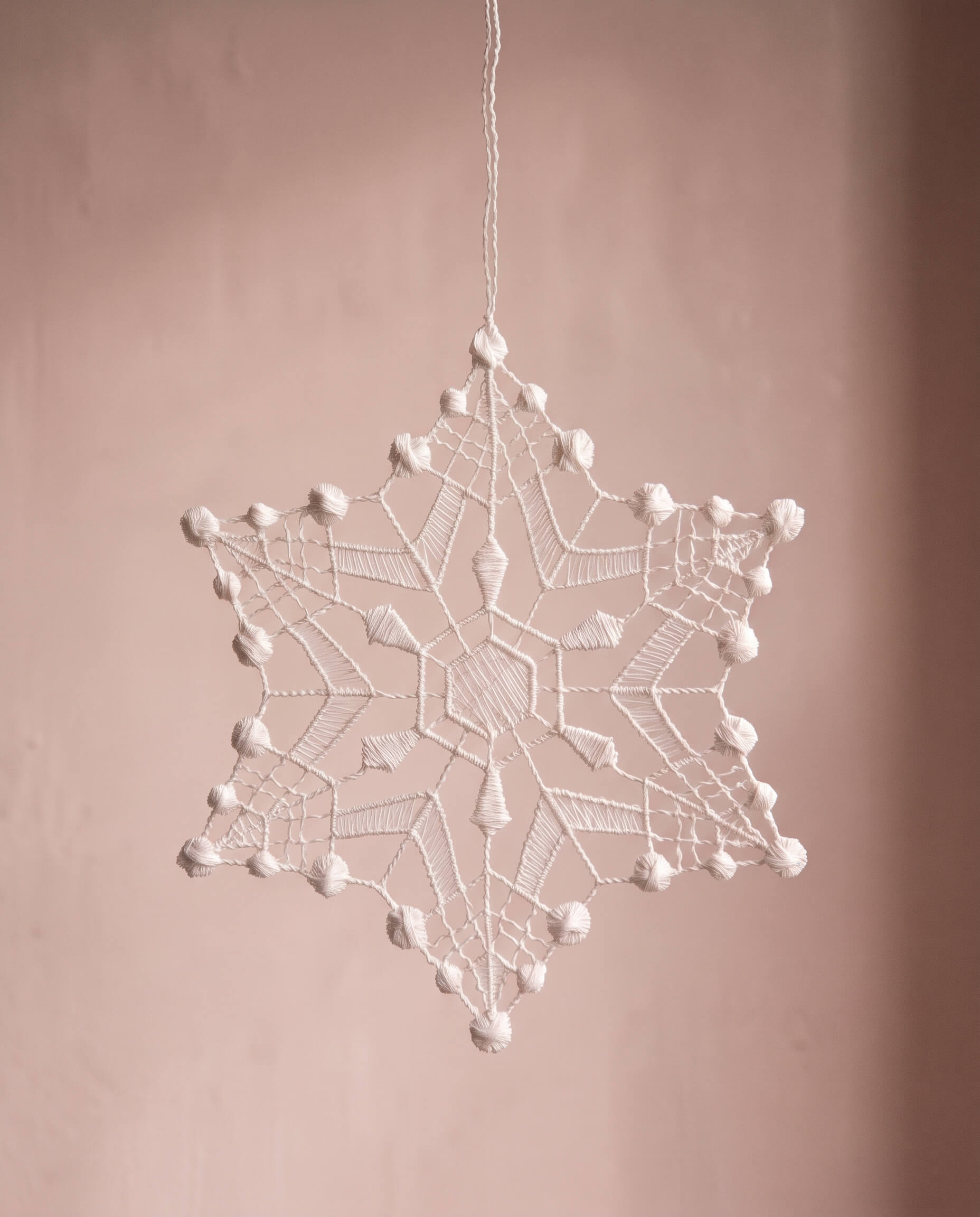 Six-point white Plauen lace snowflake ornament with dotted strands, made in Plauen, Germany