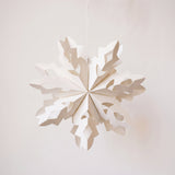 Handmade white paper cut snowflake ornament in a Scandinavian design, with a cotton hanger