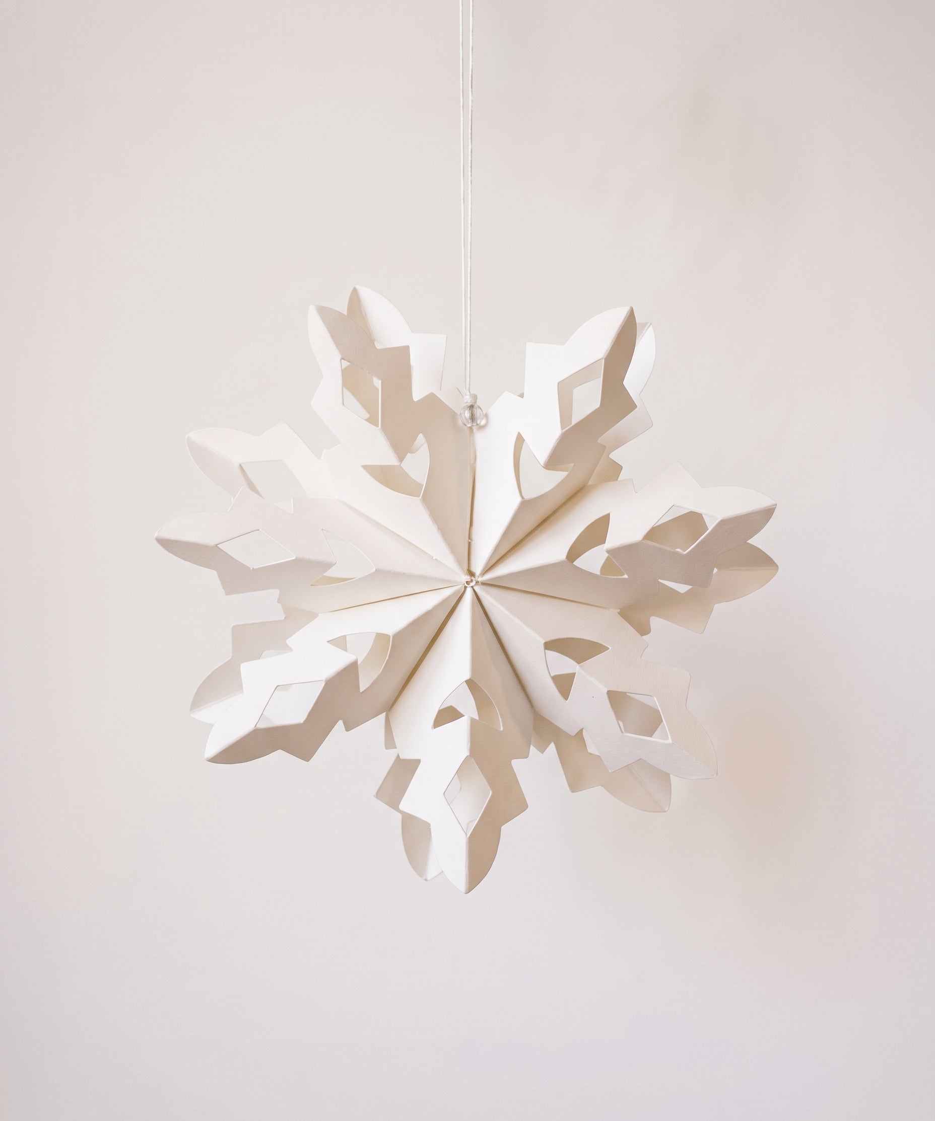 Handmade white paper cut snowflake ornament in a Scandinavian design, with a cotton hanger