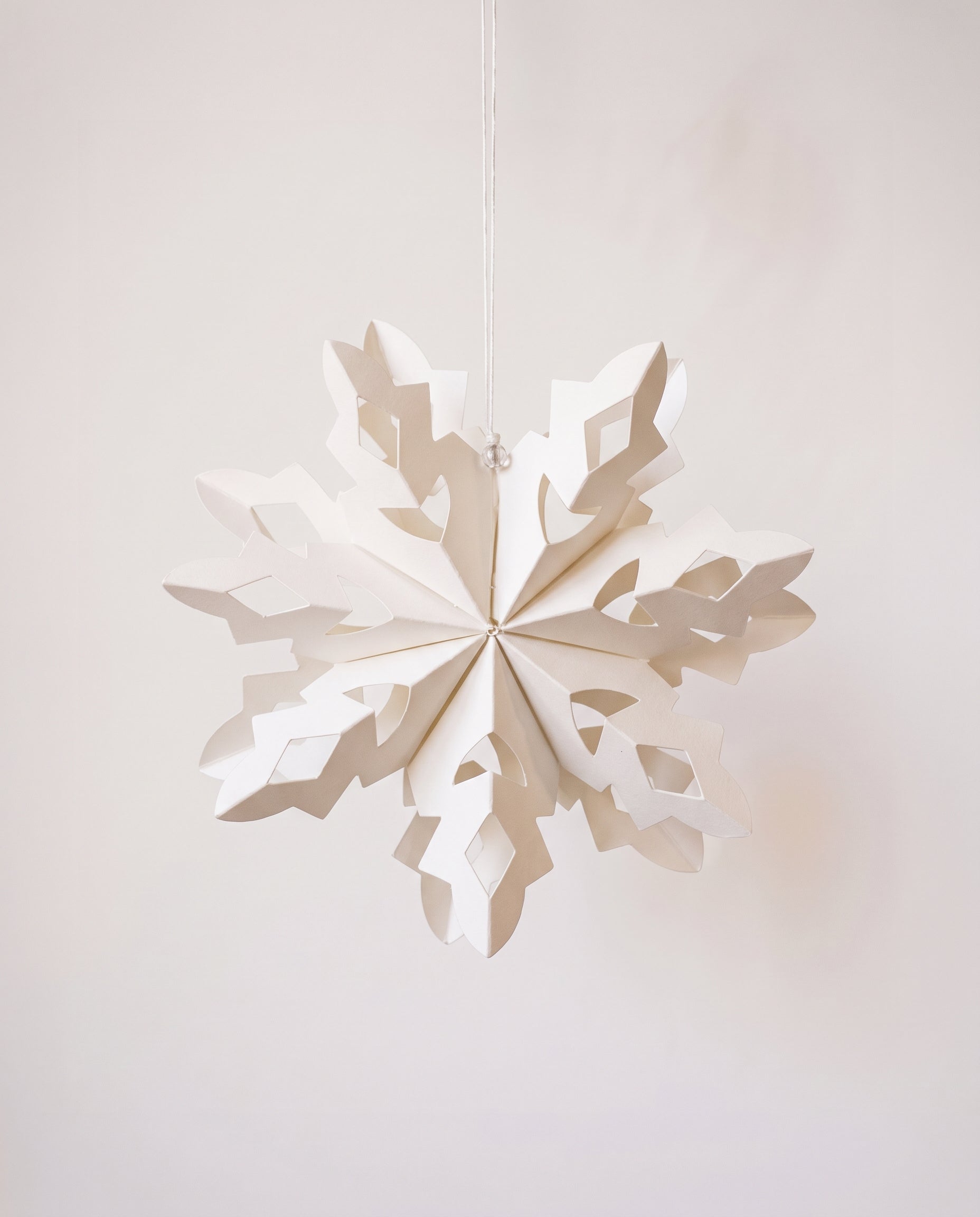 Handmade white paper cut snowflake ornament in a Scandinavian design, with a cotton hanger